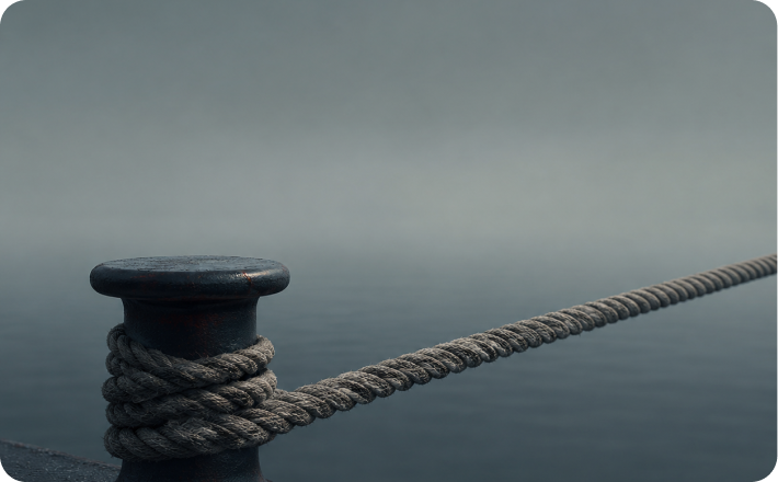 Heavy mooring rope secured to a metal bollard beside still water